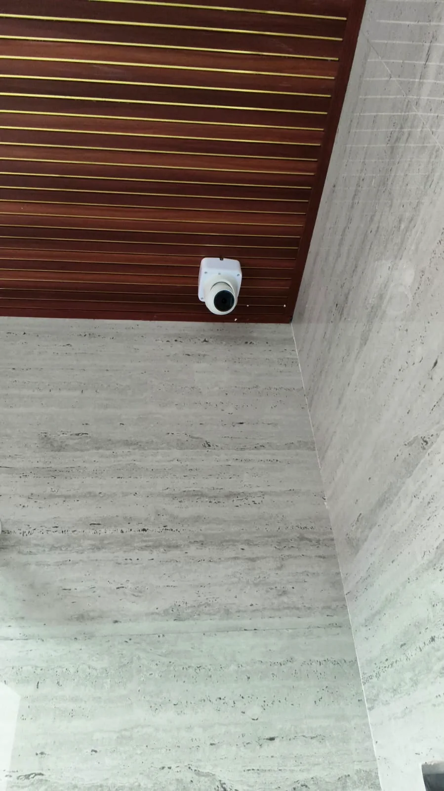 White dome CCTV camera mounted on a wood-panelled ceiling